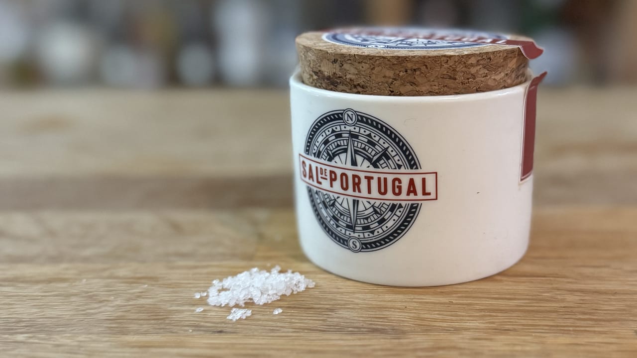 A closeup photo of a pot of fleur de sal. It has a cork lid and some grains of the salt are spilled by its base.