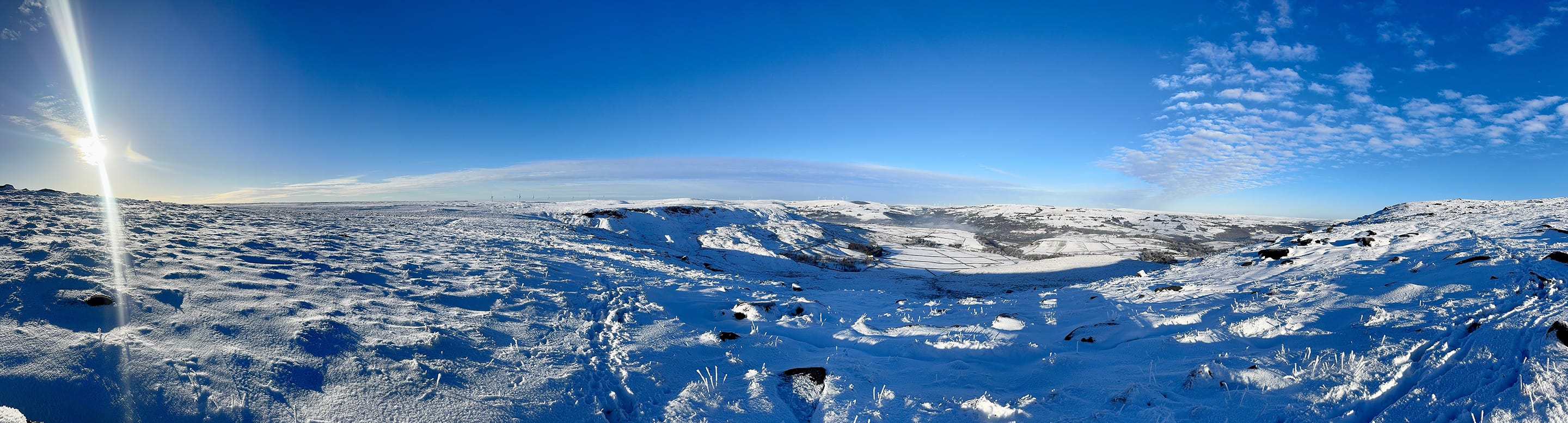 A vast panoramic photo of the snow-covered moors surrounding Stoodley Pike and its monument.